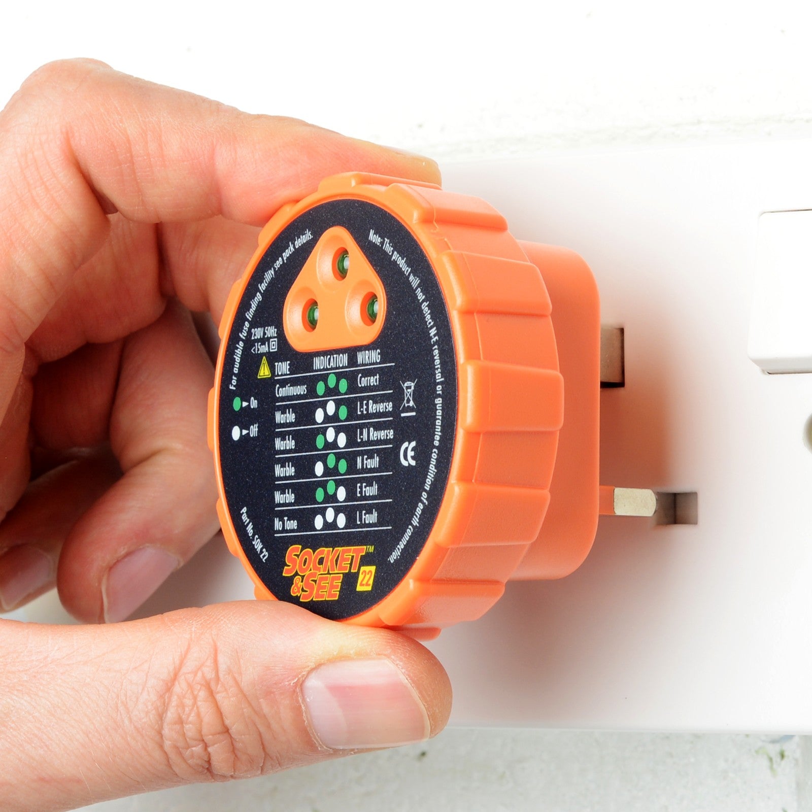 Hand holding an orange electrical tester against a wall socket.